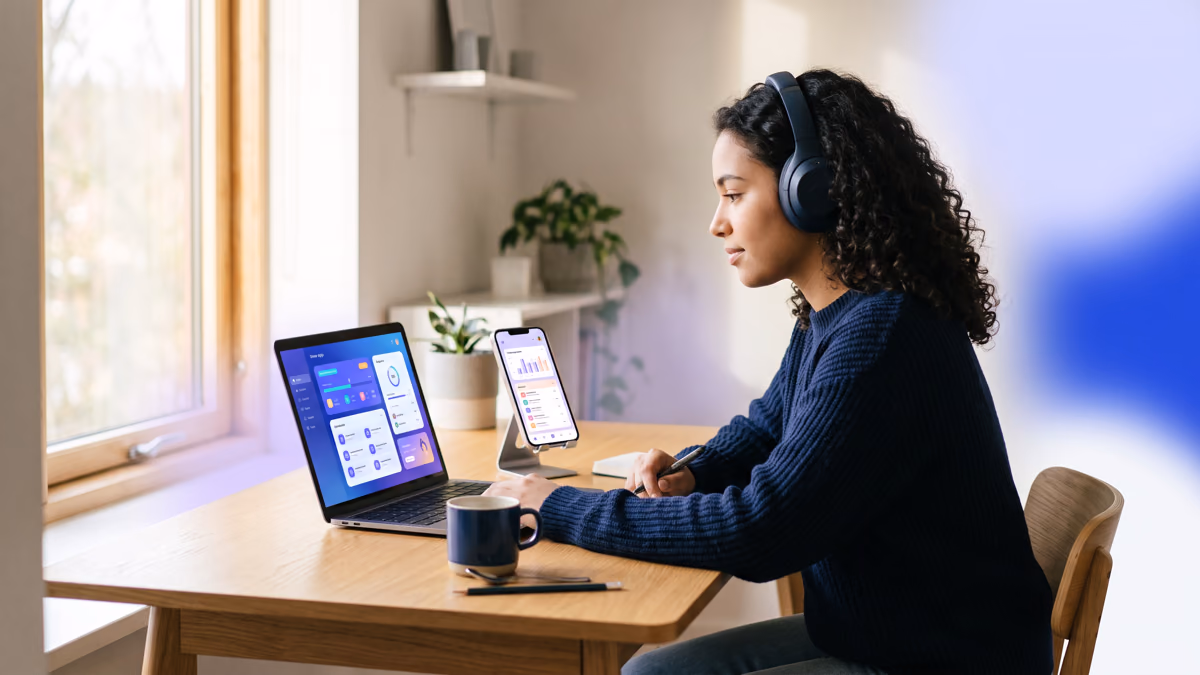 student comparing two study apps on laptop and phone while wearing headphones